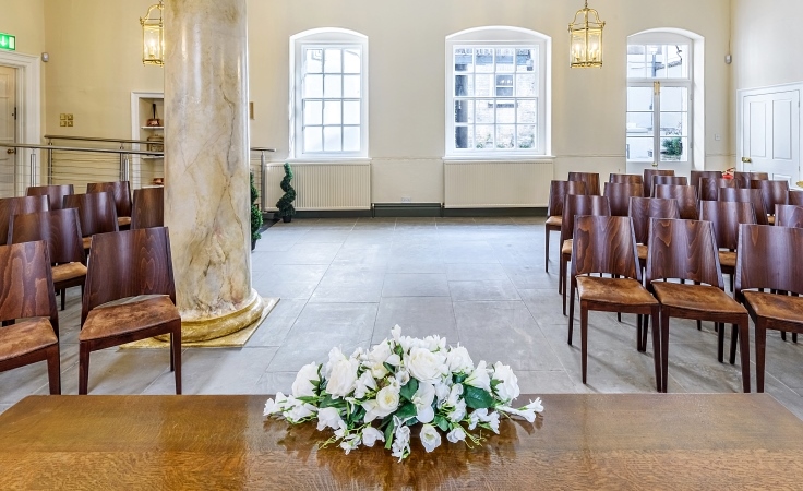 A room with chairs, a column, a tiled floor and flowers on a table.